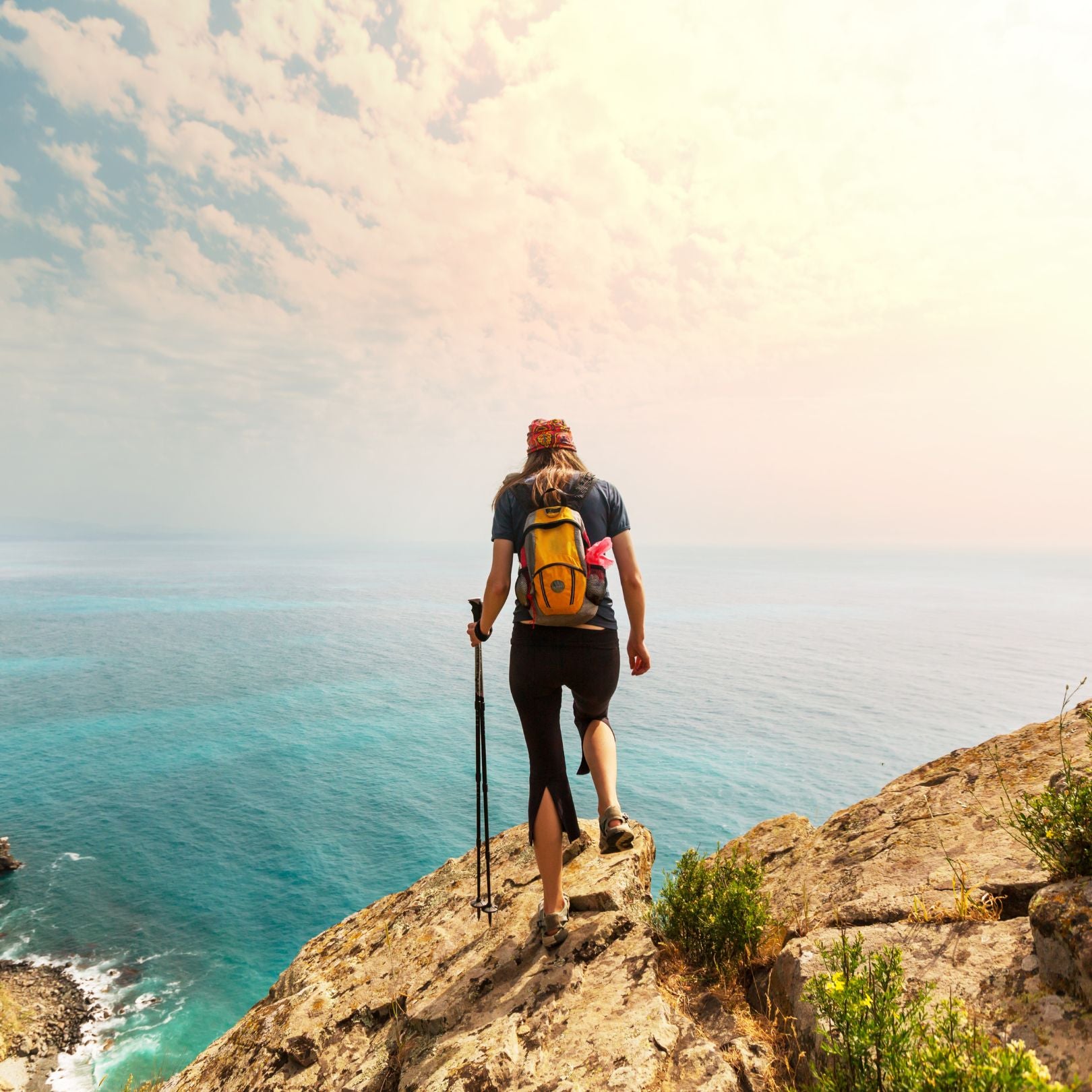 Person with a backpack and hiking poles standing on a cliff overlooking the ocean.