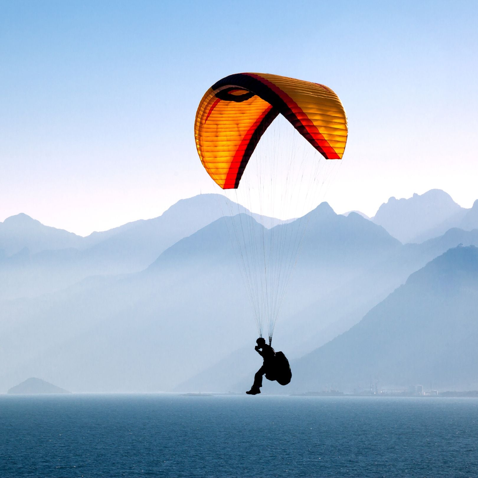 Person paragliding over water with mountains in the background